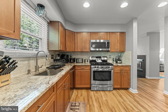 kitchen featuring a sink, tasteful backsplash, light wood-type flooring, and appliances with stainless steel finishes