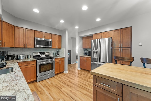 kitchen featuring brown cabinetry, stainless steel appliances, tasteful backsplash, light stone countertops, and light wood-style floors