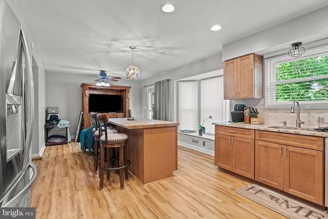 kitchen featuring light wood-style floors, a sink, stainless steel refrigerator with ice dispenser, and a breakfast bar area