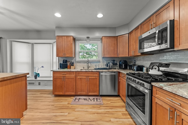 kitchen with light wood finished floors, stainless steel appliances, a sink, and decorative backsplash