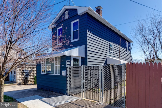 view of home's exterior featuring a fenced front yard, concrete driveway, a chimney, and a gate