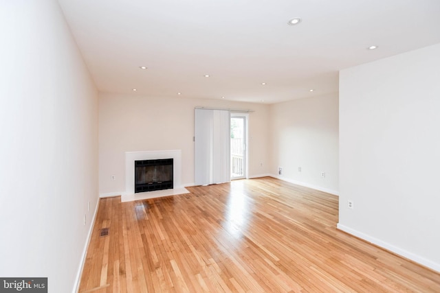 unfurnished living room featuring visible vents, a glass covered fireplace, baseboards, light wood-type flooring, and recessed lighting