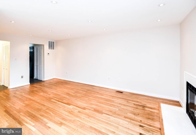unfurnished living room with baseboards, a fireplace with flush hearth, and light wood-style flooring