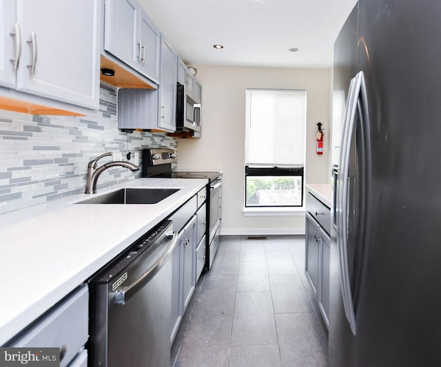 kitchen featuring appliances with stainless steel finishes, a sink, light countertops, tile patterned floors, and backsplash