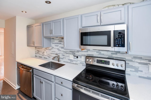 kitchen featuring decorative backsplash, light countertops, gray cabinets, a sink, and appliances with stainless steel finishes