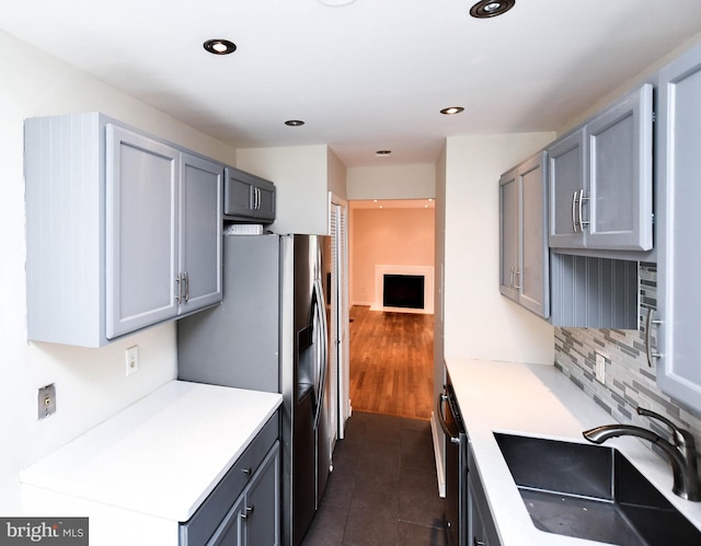 kitchen featuring a sink, stainless steel fridge with ice dispenser, backsplash, dark tile patterned floors, and gray cabinetry