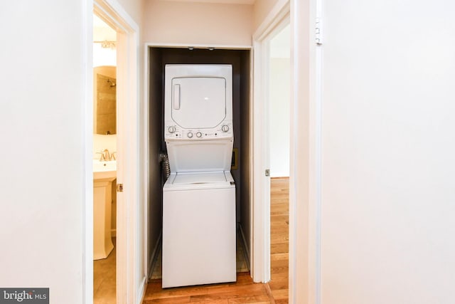 laundry room with light wood-style floors, stacked washer / dryer, and a sink