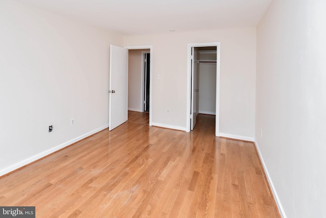 unfurnished bedroom featuring baseboards, light wood-style flooring, and a walk in closet