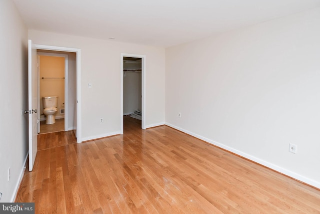 unfurnished bedroom with baseboards, a spacious closet, light wood-style flooring, and a closet