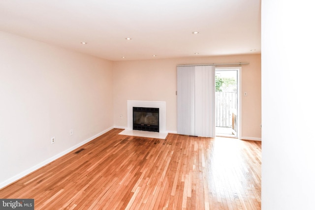 unfurnished living room featuring light wood-style floors, a fireplace with flush hearth, baseboards, and visible vents