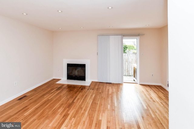 unfurnished living room featuring light wood-style floors, recessed lighting, baseboards, a fireplace with flush hearth, and visible vents