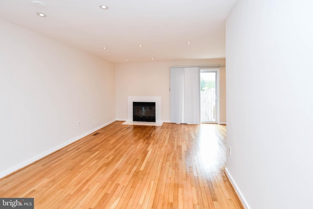 unfurnished living room featuring recessed lighting, baseboards, a fireplace with flush hearth, and light wood-style flooring