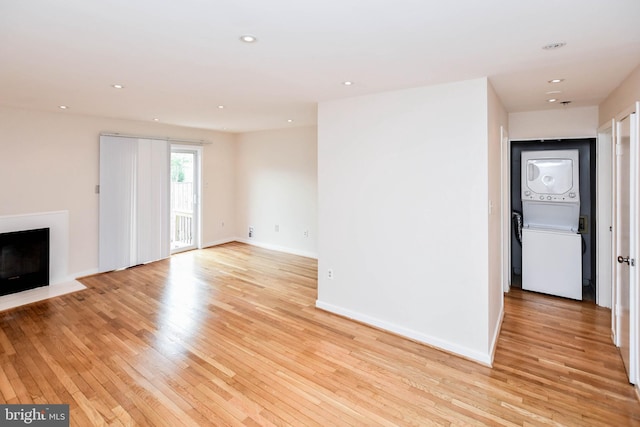 unfurnished living room with light wood-style floors, stacked washer and dryer, recessed lighting, and a fireplace