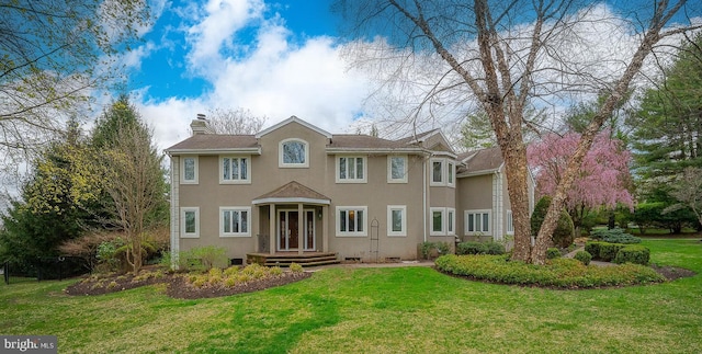view of front facade with a front yard, stucco siding, and a chimney