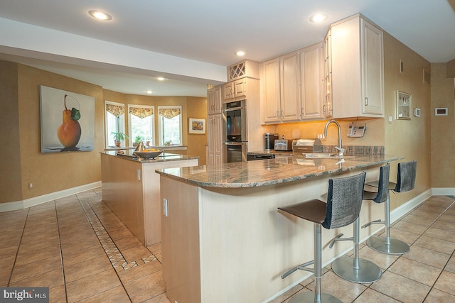 kitchen with light tile patterned floors, double oven, stone countertops, a center island, and a sink