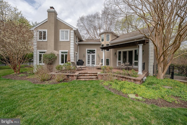 back of house with a patio area, a lawn, a chimney, stucco siding, and french doors