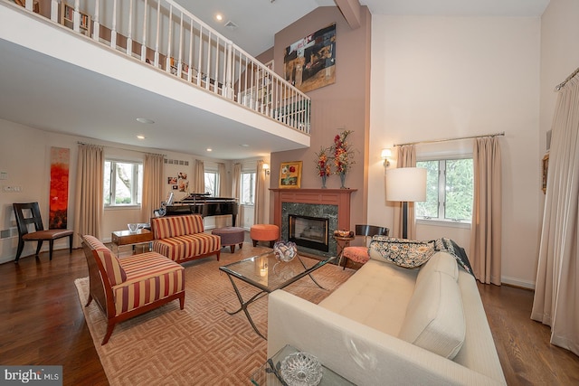living area with a premium fireplace, wood finished floors, a towering ceiling, and a wealth of natural light