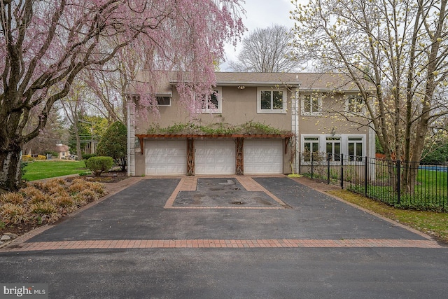 view of front facade with driveway, stucco siding, fence, and a garage