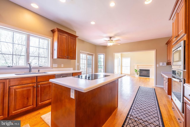 kitchen featuring a fireplace, a sink, ceiling fan, light countertops, and stainless steel appliances