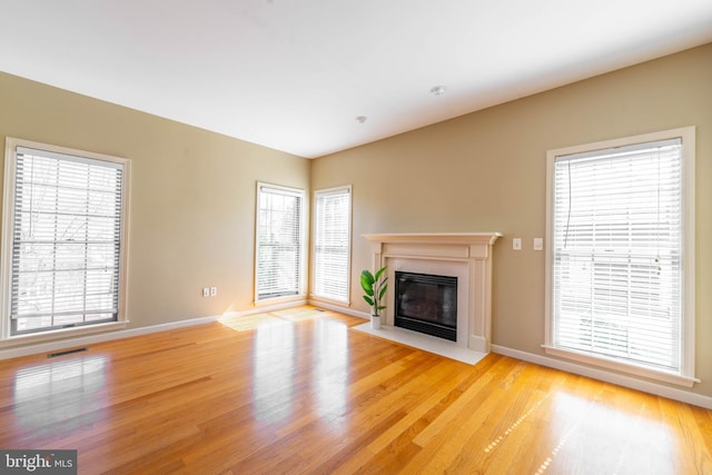unfurnished living room featuring visible vents, light wood-style flooring, baseboards, and a fireplace with flush hearth