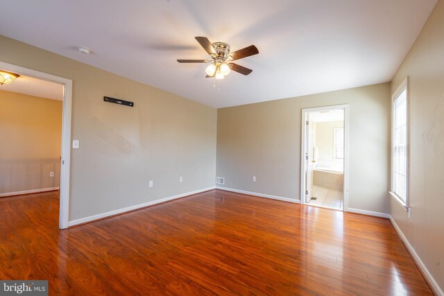unfurnished bedroom with wood finished floors, visible vents, baseboards, ceiling fan, and ensuite bathroom