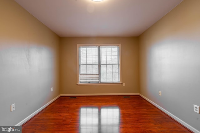 empty room featuring visible vents, wood finished floors, and baseboards