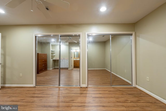 unfurnished bedroom with two closets, baseboards, recessed lighting, wood finished floors, and a ceiling fan