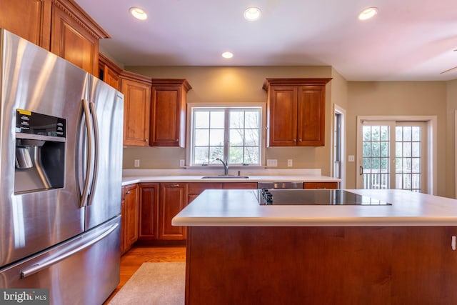 kitchen featuring black electric stovetop, stainless steel fridge with ice dispenser, light countertops, brown cabinetry, and a sink