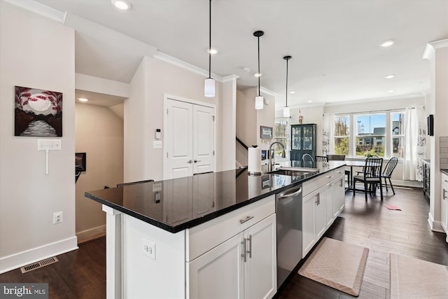 kitchen with visible vents, a sink, dark countertops, an island with sink, and stainless steel dishwasher
