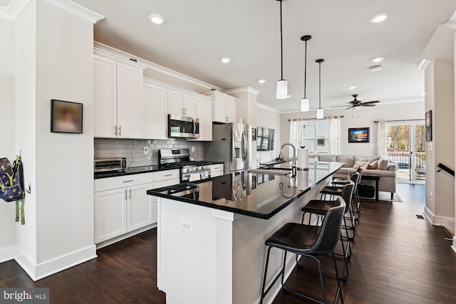kitchen with open floor plan, appliances with stainless steel finishes, dark countertops, and ornamental molding