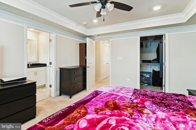 bedroom with crown molding, ensuite bathroom, a tray ceiling, light colored carpet, and a walk in closet
