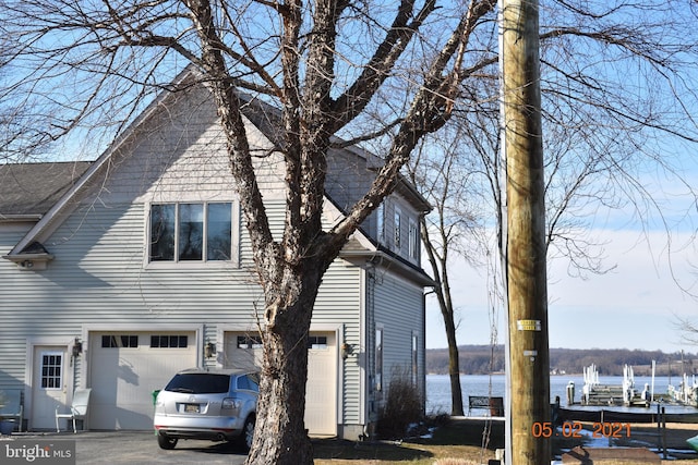 view of side of home with roof with shingles, a garage, and a water view