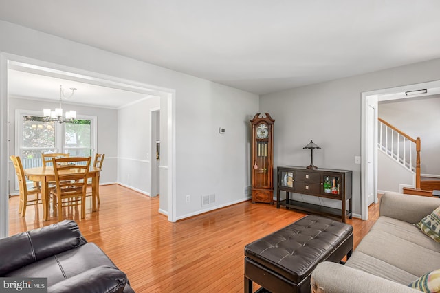 living room featuring light wood-style floors, a chandelier, baseboards, visible vents, and stairway