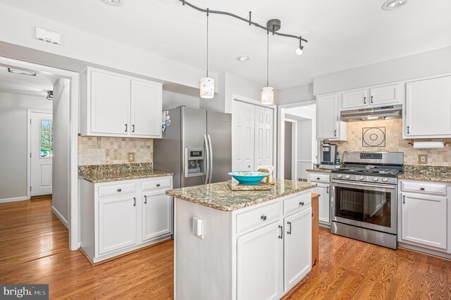 kitchen featuring backsplash, appliances with stainless steel finishes, light wood finished floors, under cabinet range hood, and white cabinetry