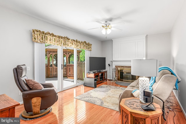 living area featuring light wood-style floors, a ceiling fan, and a fireplace