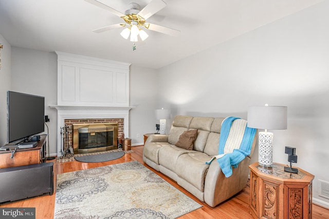living area with a brick fireplace, light wood-style flooring, a ceiling fan, baseboards, and visible vents