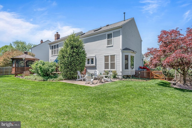 rear view of house featuring a lawn, fence, a patio, a chimney, and a gazebo
