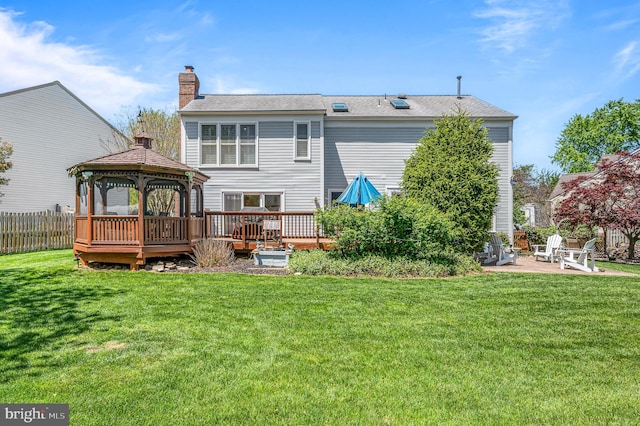 rear view of house with fence, a deck, a chimney, a gazebo, and a yard