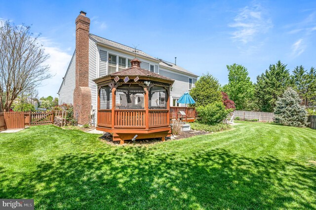 rear view of property featuring fence, a wooden deck, a gazebo, and a chimney