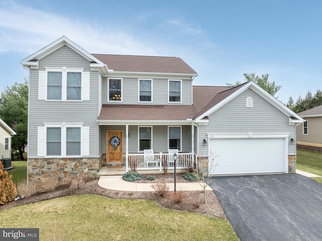 traditional-style home featuring stone siding, covered porch, driveway, and a shingled roof