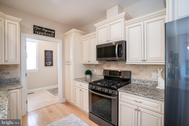 kitchen with light stone counters, baseboards, light wood finished floors, stainless steel appliances, and decorative backsplash