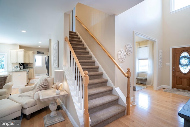 foyer entrance with stairway, baseboards, light wood-style flooring, recessed lighting, and a towering ceiling