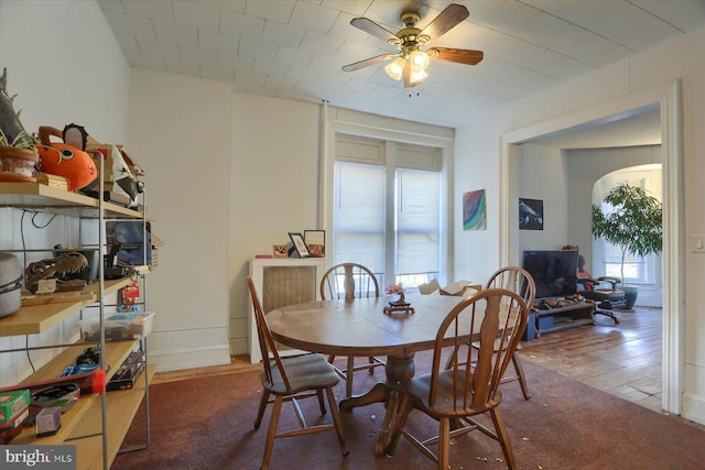 dining space with arched walkways, baseboards, a ceiling fan, and hardwood / wood-style flooring