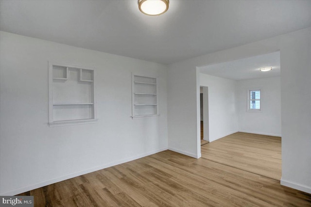 spare room with built in shelves, baseboards, and wood finished floors