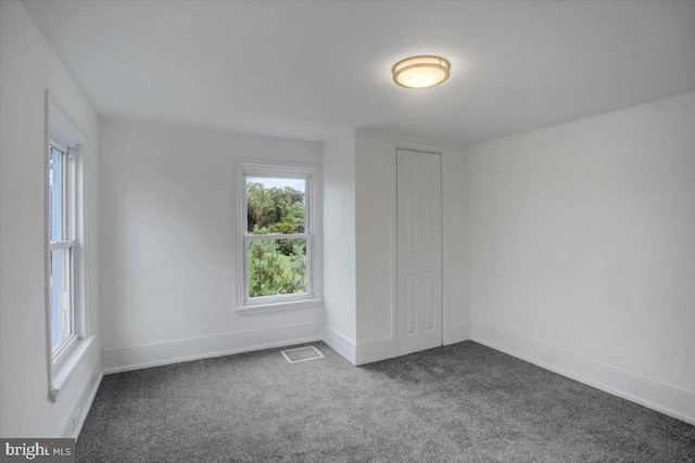 unfurnished room with dark colored carpet, visible vents, and baseboards