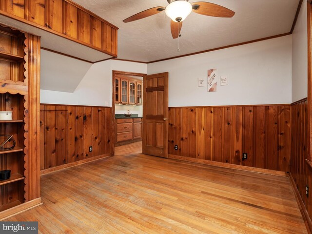 spare room with ceiling fan, wood walls, light wood-type flooring, and a wainscoted wall