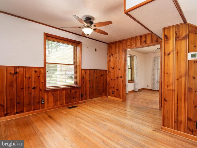 unfurnished room featuring a wainscoted wall, ceiling fan, light wood-type flooring, and wood walls