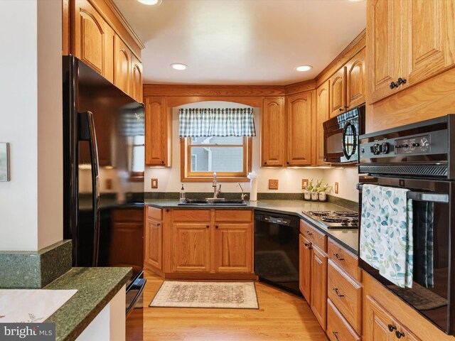 kitchen featuring a sink, dark countertops, black appliances, and light wood-style flooring