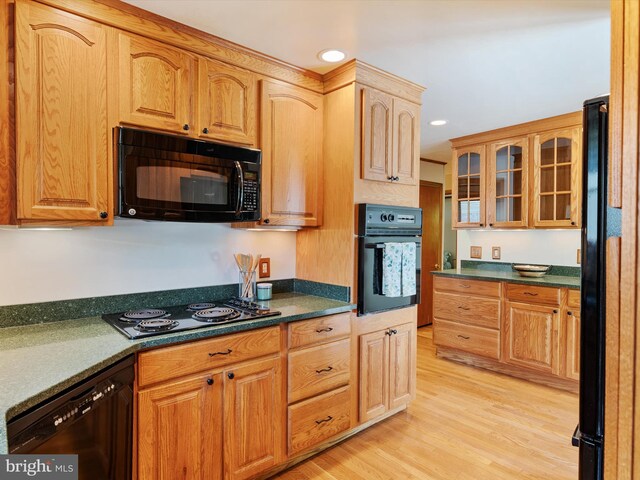 kitchen featuring light wood-type flooring, black appliances, dark countertops, and glass insert cabinets