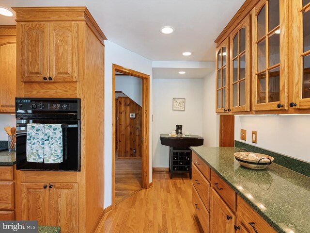 kitchen with glass insert cabinets, light wood finished floors, dark stone countertops, and oven